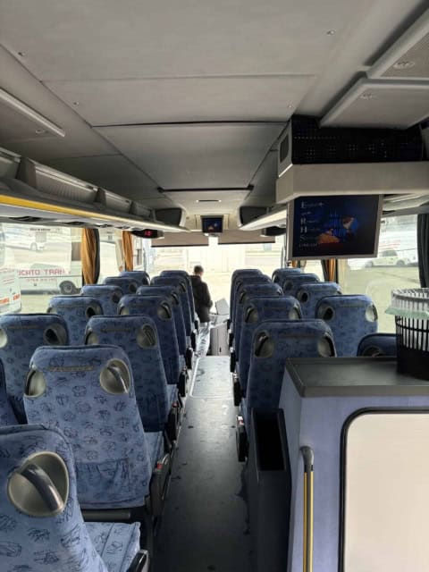 Interiorul autocarului de 50 de locuri, spre față: scaune albastre, culoar central și monitoare TV
