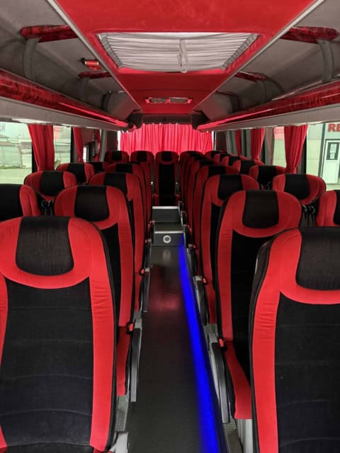Interiorul microbuzului de 30 de locuri: scaune din catifea roșie cu negru, culoar iluminat și perdele roșii